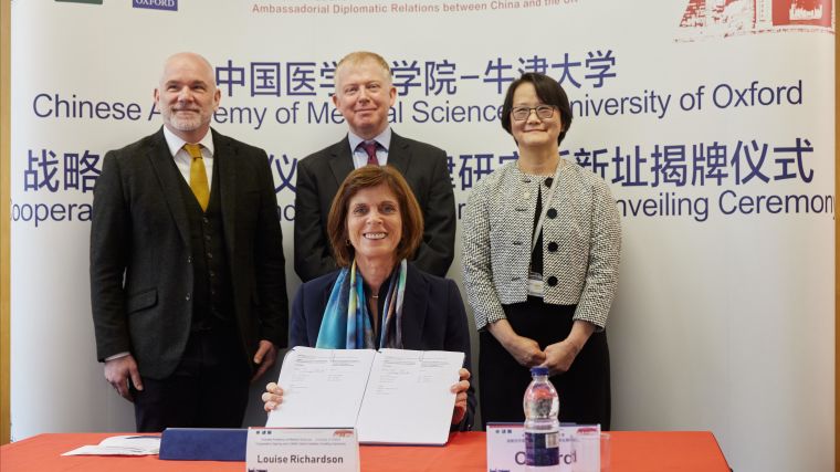 The VC of Oxford sat signing the agreement with members of COI stood behind her